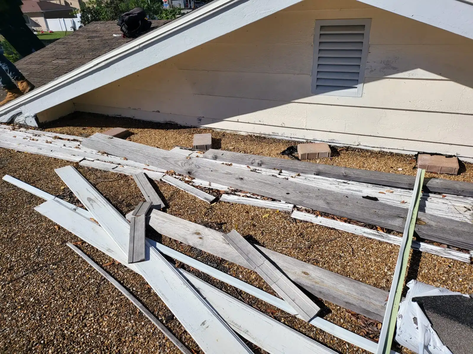 Damaged wooden boards and loose planks are scattered on a shingled roof beneath the eaves of a house—an issue easily fixed by Skyview Roofing, providers of the BEST ROOFING SERVICES IN FLORIDA.