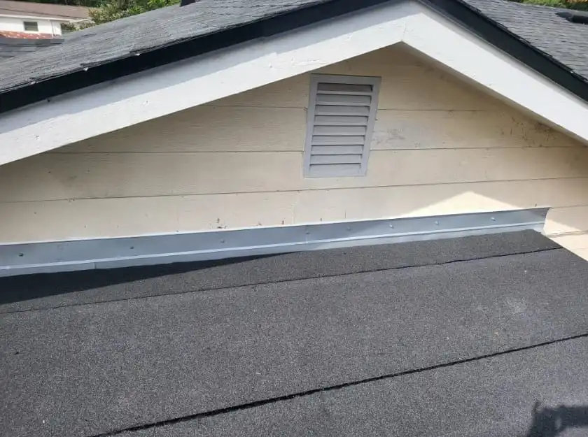 A close-up view of a house roof by Skyview Roofing, showing asphalt shingles, metal flashing, beige siding, and a small vent on the gable end—quality details you expect from the Best Roofing Florida has to offer.